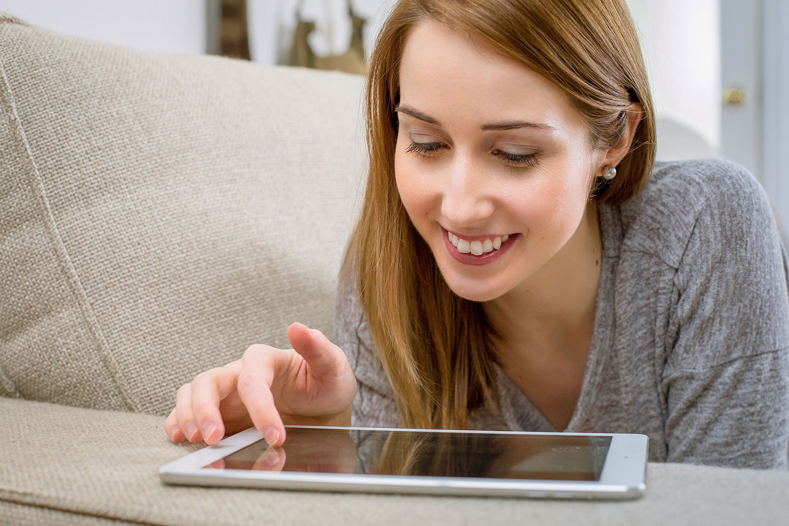 Frau liegt auf der Couch, bedient Tablet